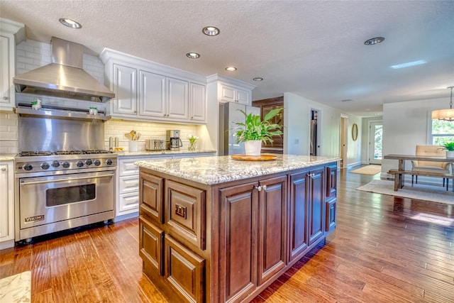 kitchen with hardwood / wood-style floors, wall chimney exhaust hood, white cabinetry, tasteful backsplash, and premium range