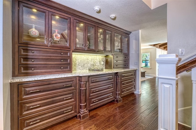 bar featuring baseboards, a textured ceiling, dark wood finished floors, and backsplash