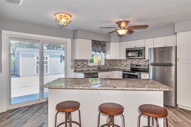 3045 Stratford Dr, Largo, FL 33771 - kitchen with white cabinets, stainless steel appliances, backsplash, wood tiled floor, and a breakfast bar area