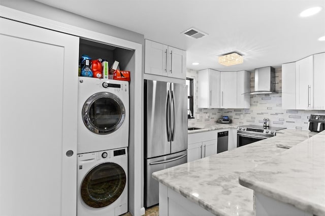 105 4th Ave NE Unit 219, Saint Petersburg, FL 33701 - kitchen with visible vents, stacked washing maching and dryer, wall chimney range hood, white cabinetry, and appliances with stainless steel finishes