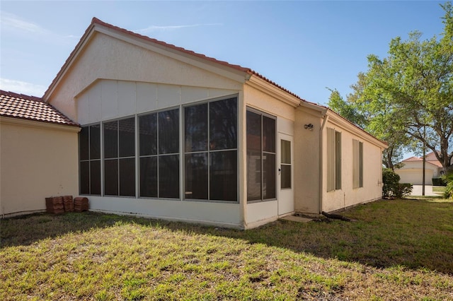 view of side of property with a sunroom, stucco siding, a tile roof, and a lawn