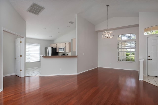 unfurnished living room with visible vents, wood finished floors, lofted ceiling, baseboards, and a notable chandelier