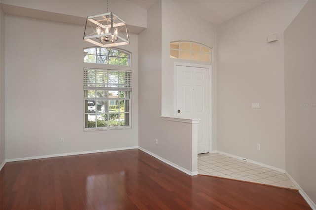 unfurnished room with wood finished floors, an inviting chandelier, baseboards, and lofted ceiling