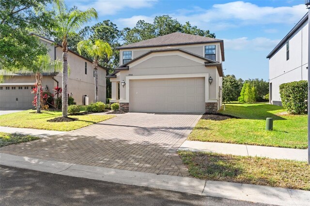 traditional-style house with a front yard, stone siding, a garage, stucco siding, and decorative driveway
