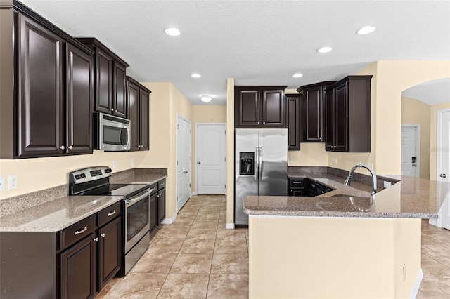 kitchen featuring arched walkways, a peninsula, stone counters, a sink, and stainless steel appliances