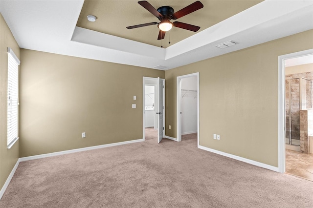 unfurnished bedroom with visible vents, baseboards, a spacious closet, carpet, and a tray ceiling