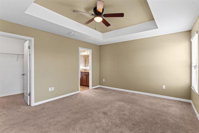 unfurnished bedroom featuring a spacious closet, a raised ceiling, carpet, and baseboards