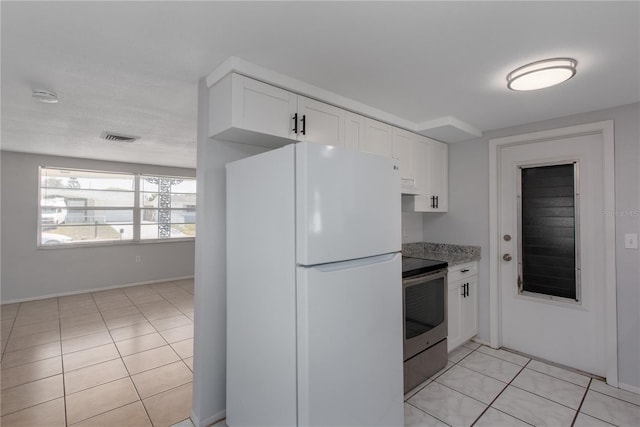 kitchen with freestanding refrigerator, light tile patterned floors, visible vents, white cabinets, and stainless steel electric range