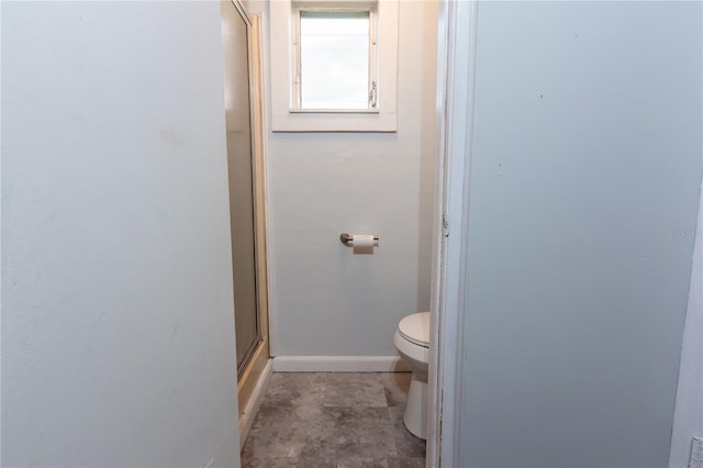 bathroom featuring a shower with door, baseboards, and toilet