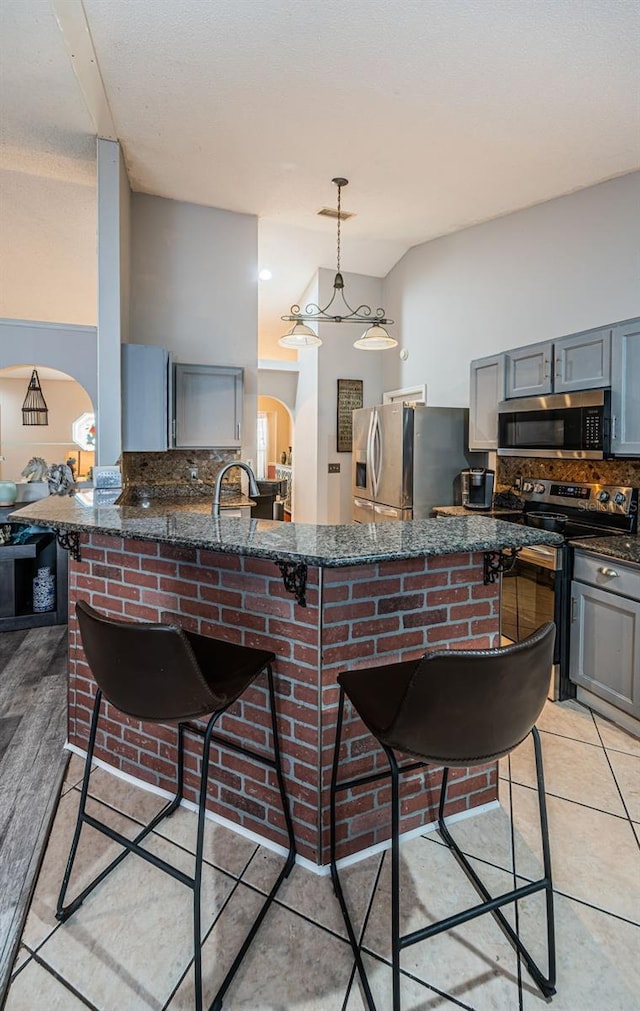 kitchen featuring gray cabinets, tasteful backsplash, a kitchen breakfast bar, and stainless steel appliances