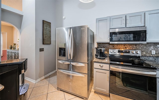 kitchen featuring light tile patterned floors, dark stone counters, decorative backsplash, arched walkways, and appliances with stainless steel finishes
