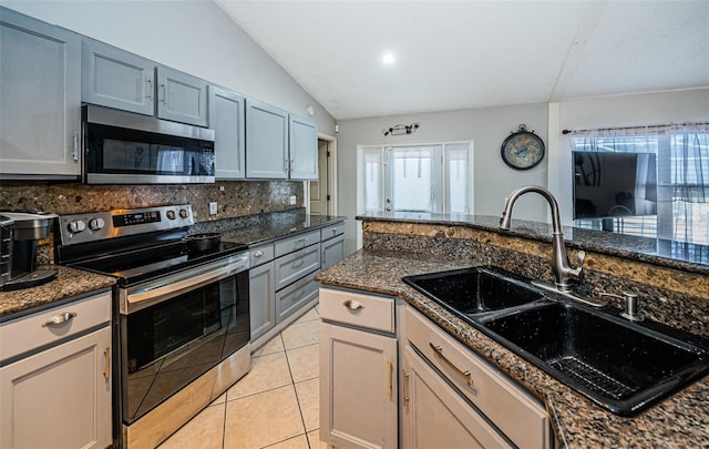kitchen featuring vaulted ceiling, backsplash, dark stone counters, stainless steel appliances, and a sink