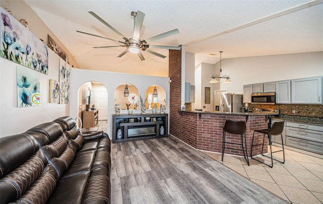 living area featuring a ceiling fan, arched walkways, a glass covered fireplace, and lofted ceiling