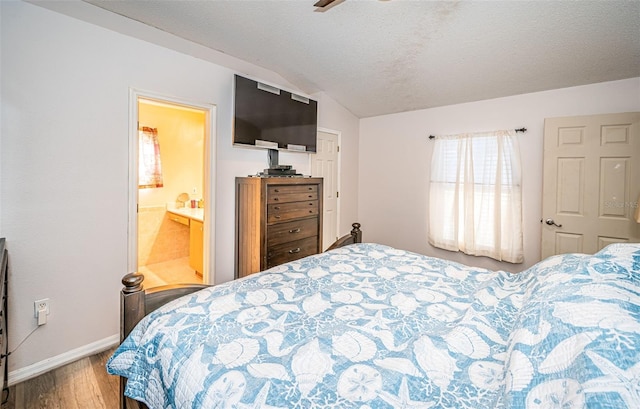 bedroom with baseboards, connected bathroom, vaulted ceiling, and wood finished floors