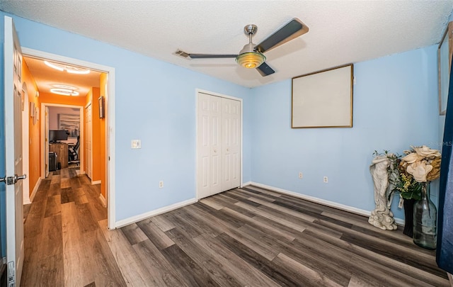 unfurnished bedroom featuring a closet, baseboards, dark wood-style floors, a textured ceiling, and a ceiling fan