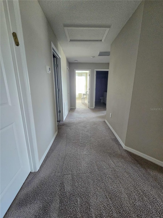 hallway featuring light carpet, visible vents, baseboards, and attic access