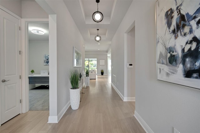 hall with baseboards, light wood-type flooring, and a raised ceiling