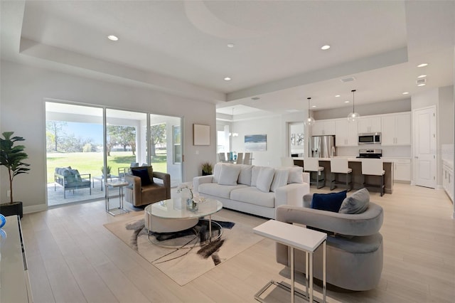 living room with a raised ceiling, light wood-style floors, and recessed lighting