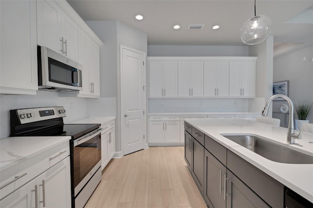 kitchen featuring decorative light fixtures, a sink, appliances with stainless steel finishes, white cabinetry, and light wood finished floors