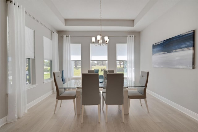 dining area featuring a chandelier, light wood-type flooring, a tray ceiling, and baseboards