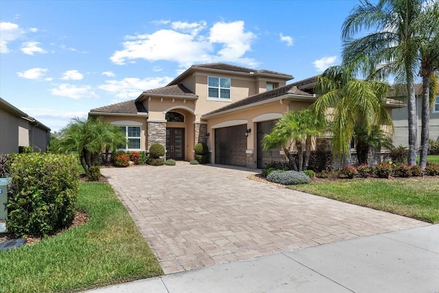 mediterranean / spanish-style home featuring stucco siding, stone siding, decorative driveway, a garage, and a tiled roof
