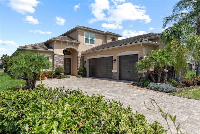 mediterranean / spanish-style house featuring an attached garage, stone siding, decorative driveway, and stucco siding
