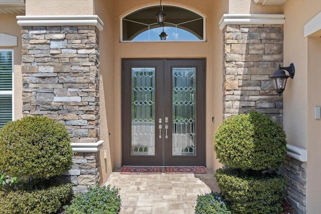 view of exterior entry with french doors, stone siding, and stucco siding