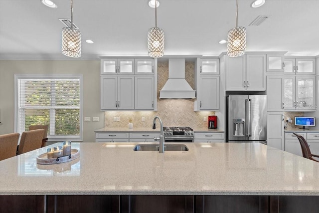 kitchen with tasteful backsplash, premium range hood, a kitchen island with sink, a sink, and premium appliances