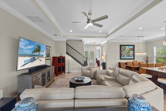 living area with baseboards, stairs, visible vents, a raised ceiling, and ceiling fan with notable chandelier
