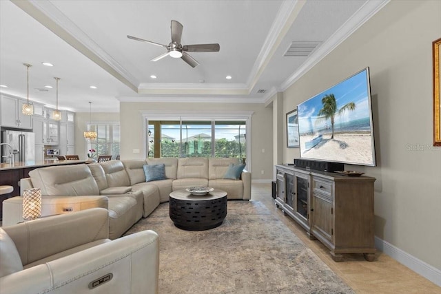 living room with baseboards, a ceiling fan, ornamental molding, and a raised ceiling