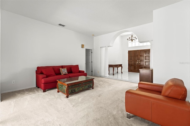 carpeted living room featuring arched walkways, visible vents, ornate columns, and an inviting chandelier