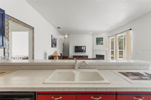 kitchen with visible vents, a sink, open floor plan, dishwashing machine, and a glass covered fireplace