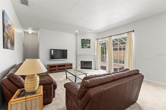 living area featuring a glass covered fireplace, baseboards, light carpet, a textured ceiling, and visible vents