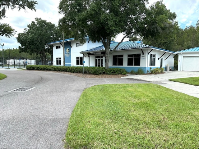 view of front facade featuring curved driveway, metal roof, a front lawn, and stucco siding
