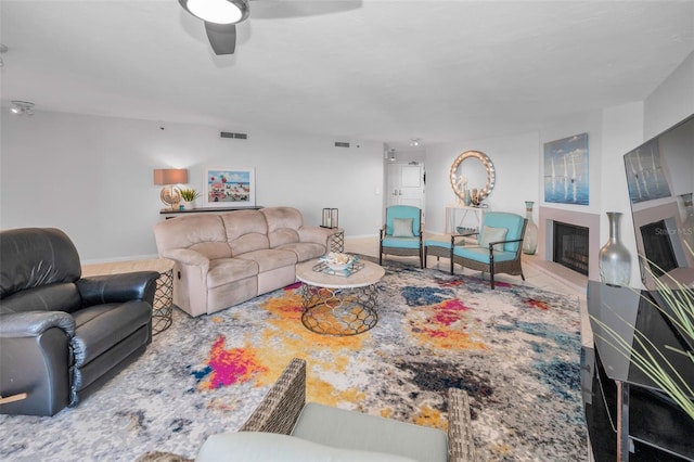 living area featuring a fireplace with raised hearth, visible vents, baseboards, and ceiling fan