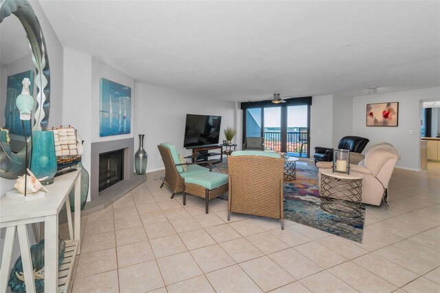 living area featuring baseboards, light tile patterned floors, ceiling fan, and a fireplace with raised hearth