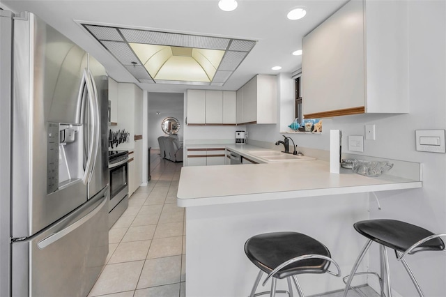 kitchen featuring light tile patterned floors, a sink, light countertops, a peninsula, and stainless steel appliances