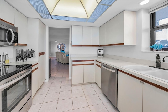 kitchen featuring light tile patterned floors, white cabinetry, appliances with stainless steel finishes, light countertops, and a sink