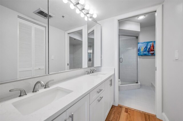 bathroom with a stall shower, double vanity, a sink, and visible vents
