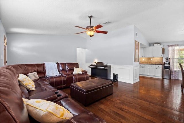 living room with a ceiling fan, lofted ceiling, dark wood-type flooring, and wainscoting