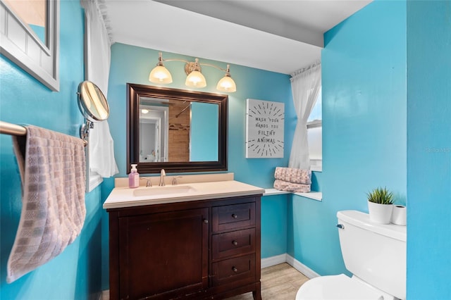 half bath with toilet, wood finished floors, vanity, and baseboards