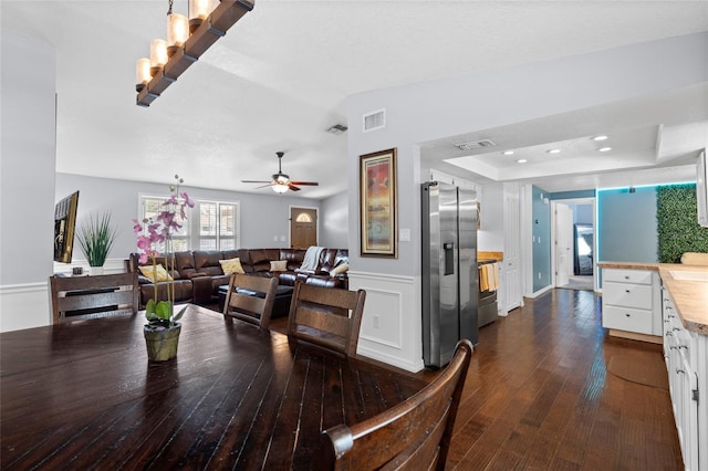 dining area with ceiling fan, dark wood-type flooring, wainscoting, and a tray ceiling