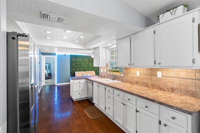 kitchen with a sink, appliances with stainless steel finishes, a textured ceiling, tasteful backsplash, and dark wood finished floors