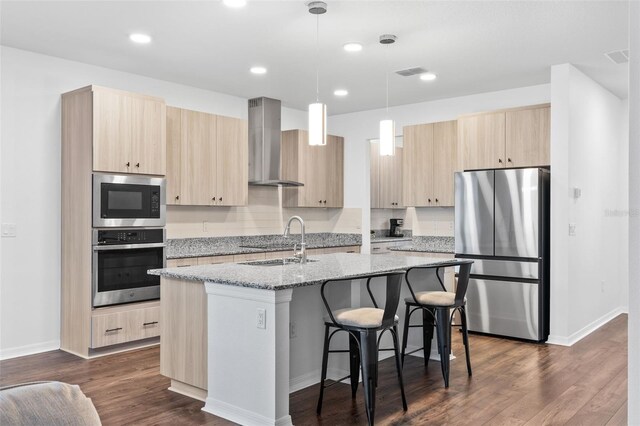 kitchen featuring wall chimney range hood, a sink, light brown cabinetry, and appliances with stainless steel finishes