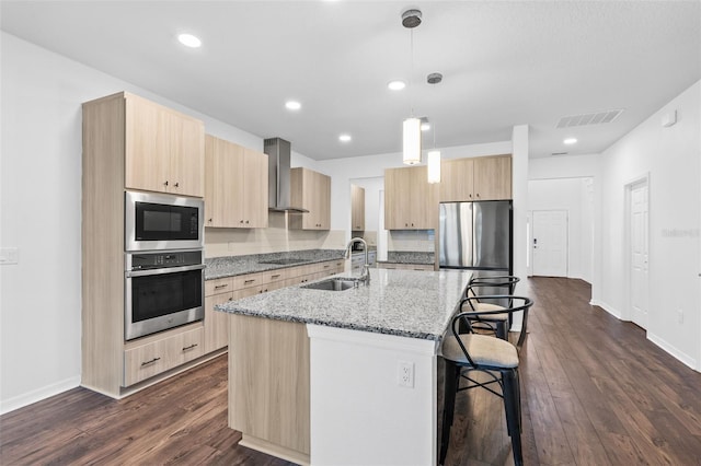 kitchen with light brown cabinets, appliances with stainless steel finishes, a sink, and wall chimney exhaust hood
