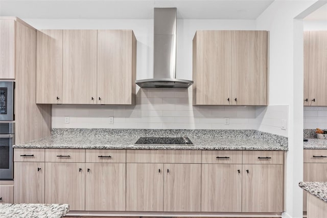 kitchen with wall chimney exhaust hood, light stone countertops, black electric stovetop, light brown cabinets, and backsplash