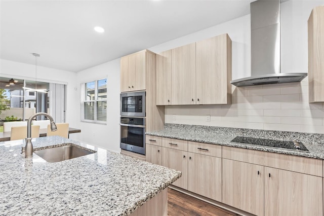 kitchen with a sink, wall chimney range hood, appliances with stainless steel finishes, light brown cabinetry, and light stone counters