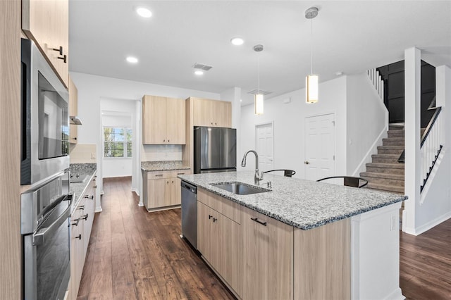 kitchen with dark wood finished floors, light stone countertops, appliances with stainless steel finishes, a sink, and light brown cabinets