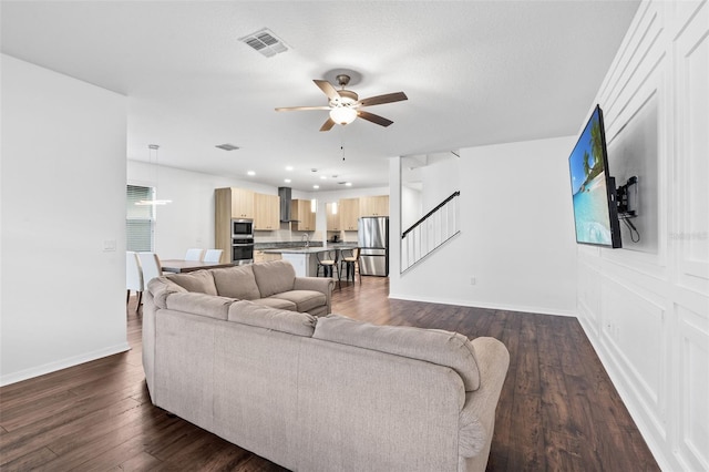 living room with ceiling fan, dark wood-type flooring, visible vents, stairway, and baseboards