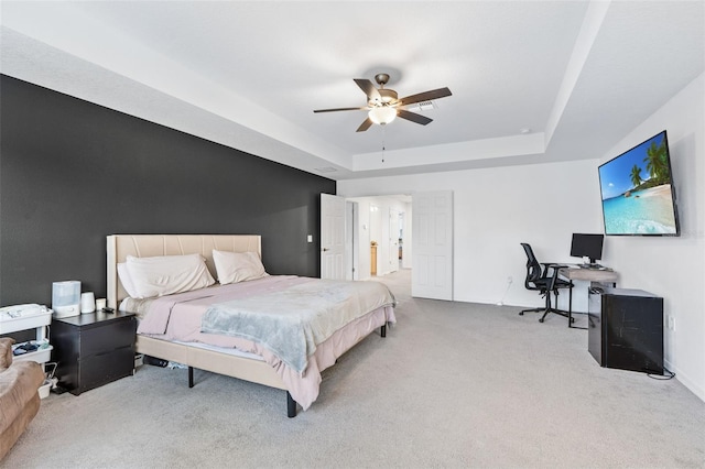 carpeted bedroom with a raised ceiling and a ceiling fan